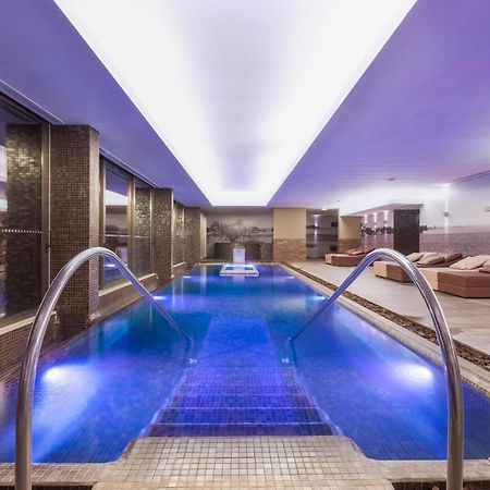 Ap Lago Montargil - Conference & Spa Eksteriør billede The photo shows a modern indoor swimming pool area. The pool features a sleek design with steps leading into the water and a gentle curve at the sides. The water is illuminated in a blue hue, enhancing the relaxing atmosphere. Surrounding the pool ar
