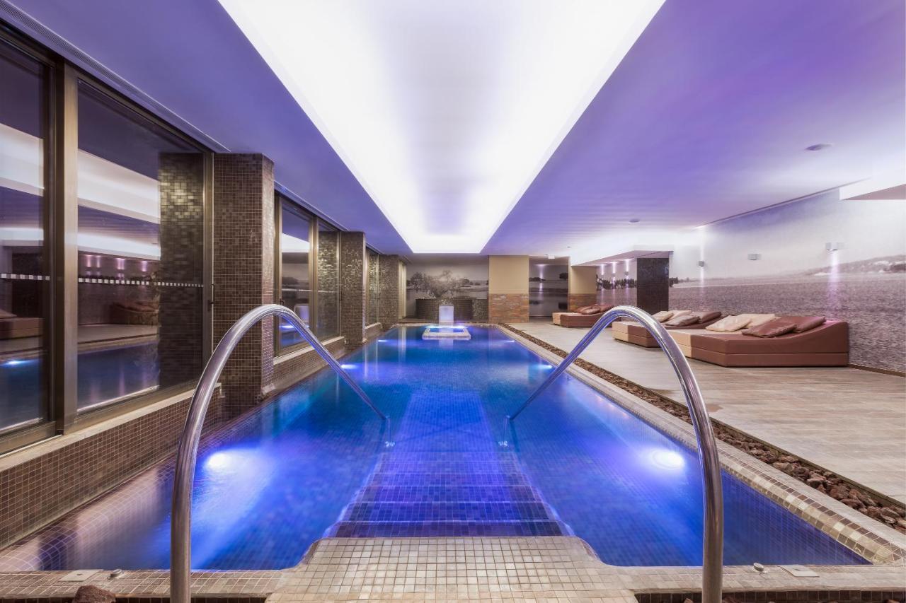 Ap Lago Montargil - Conference & Spa Eksteriør billede The photo shows a modern indoor swimming pool area. The pool features a sleek design with steps leading into the water and a gentle curve at the sides. The water is illuminated in a blue hue, enhancing the relaxing atmosphere. Surrounding the pool ar