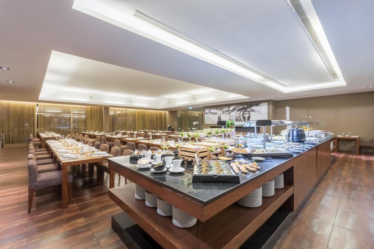 Ap Lago Montargil - Conference & Spa Eksteriør billede The photo displays a spacious restaurant interior, featuring a well-organized dining area with multiple tables set for patrons. In the center, there is a large buffet station filled with an array of food items. The decor is modern and elegant, with w