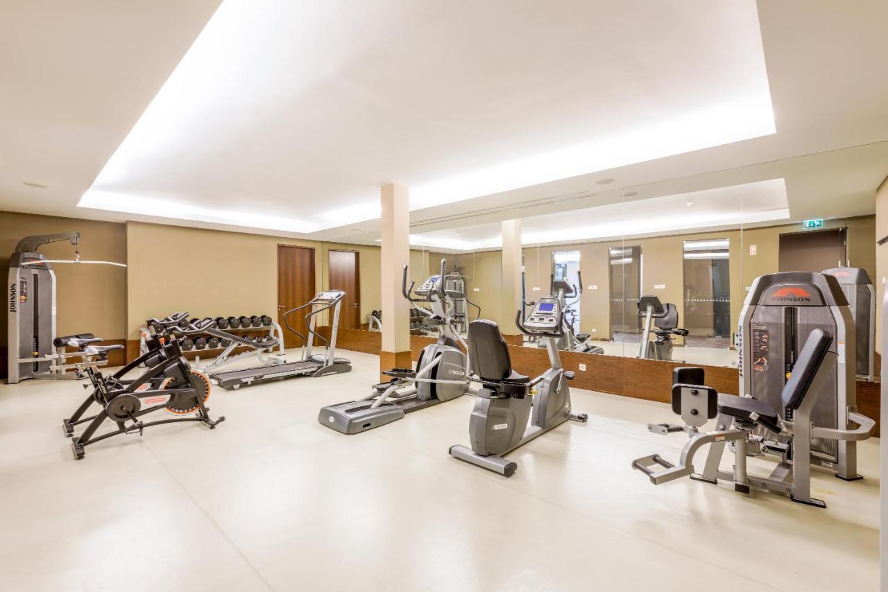 Ap Lago Montargil - Conference & Spa Eksteriør billede The image shows a modern gym interior featuring various exercise equipment. On the left, there are free weights and weight benches. In the center, there are multiple machines, including a stationary bike and an elliptical. The space is well-lit with 