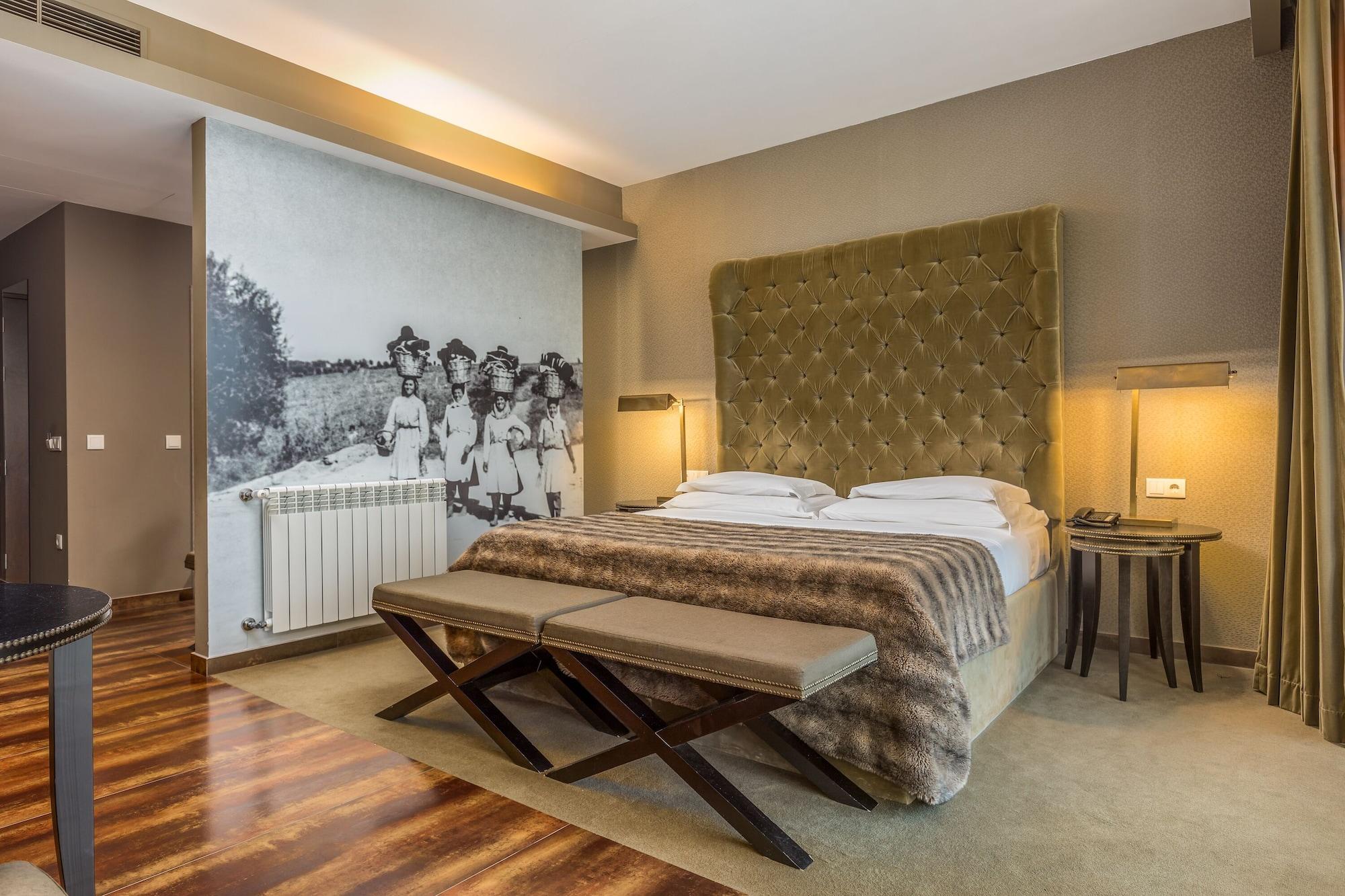 Ap Lago Montargil - Conference & Spa Eksteriør billede The photo shows a modern hotel room with a large, plush bed that has a tufted, green headboard. The bedding is white with a textured blanket at the foot of the bed. A decorative wall behind the bed features a black and white mural of children in a fi