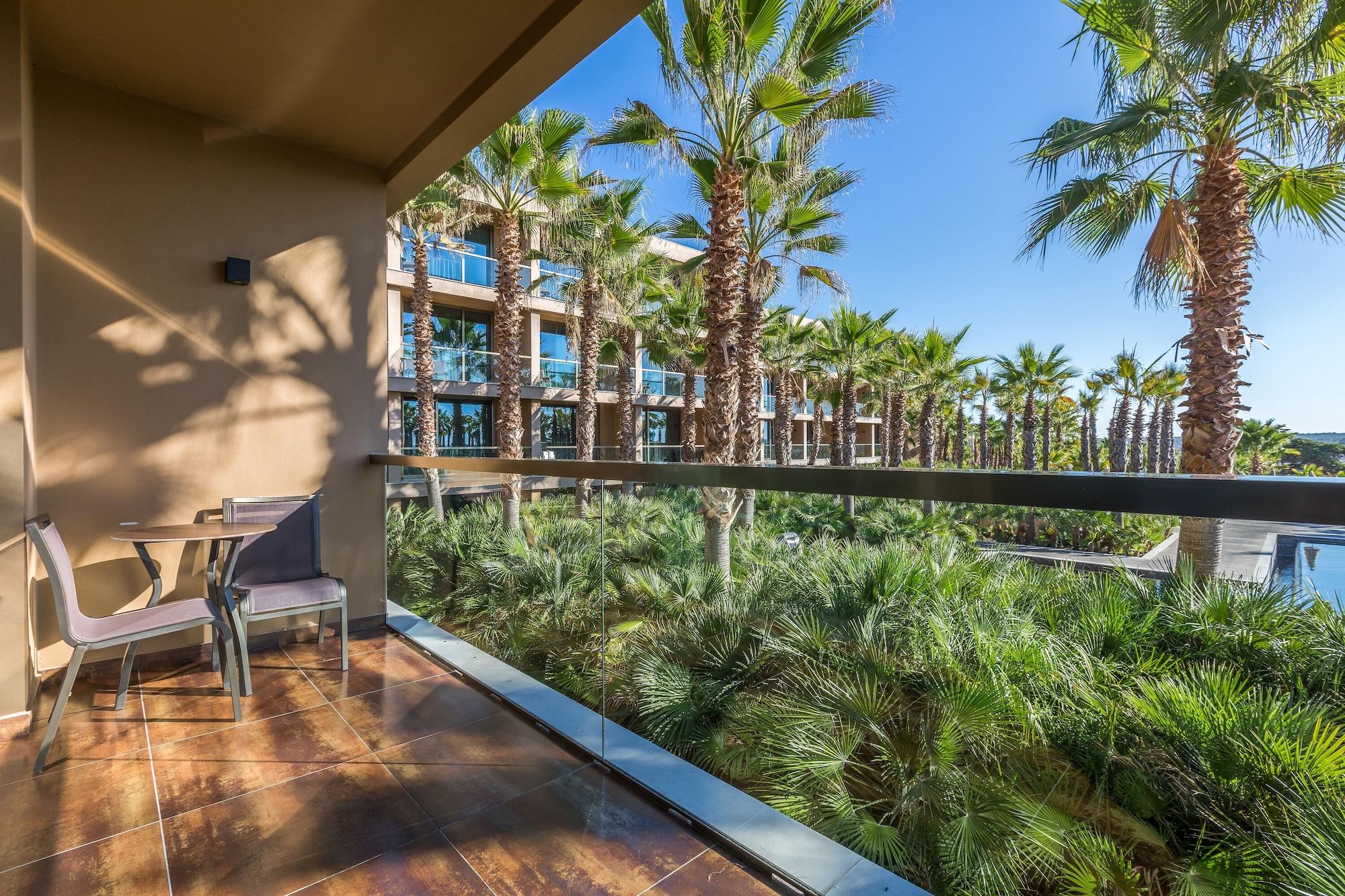 Ap Lago Montargil - Conference & Spa Eksteriør billede The photo shows a balcony with modern furniture, including a chair and a small table. In the background, there are tall palm trees and lush greenery, suggesting a tropical or resort-like setting. The buildings in the distance are likely part of a hot