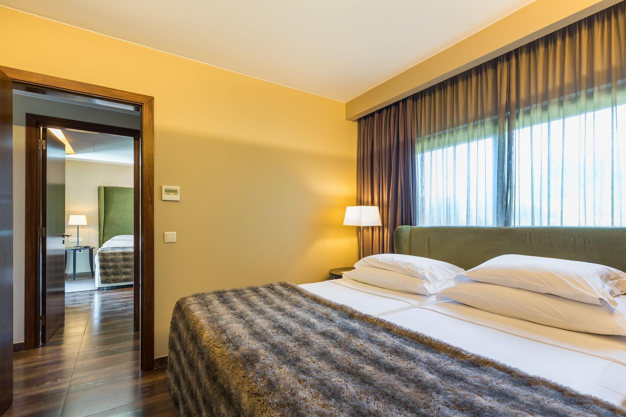Ap Lago Montargil - Conference & Spa Eksteriør billede The photo shows the interior of a well-furnished hotel room. It features two beds with white linens and a gray decorative throw on top. The walls are painted a warm yellow, and there are floor-to-ceiling windows covered with dark curtains that allow 