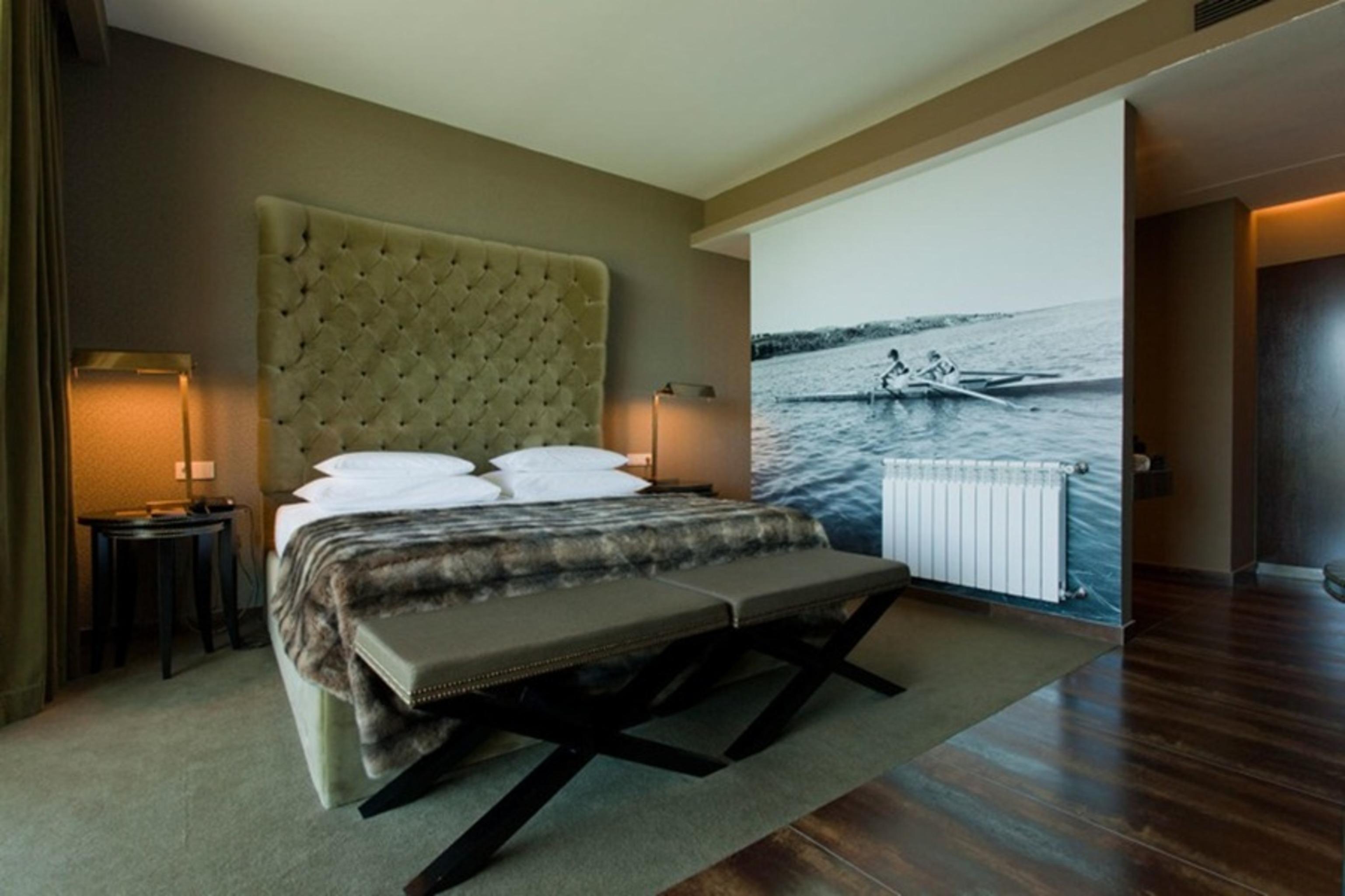 Ap Lago Montargil - Conference & Spa Eksteriør billede The photo shows a modern hotel room featuring a large bed with a tufted headboard and plush bedding. The color palette is neutral, with shades of green and gray. On one side of the room, there are bedside tables with lamps. A comfortable bench sits a