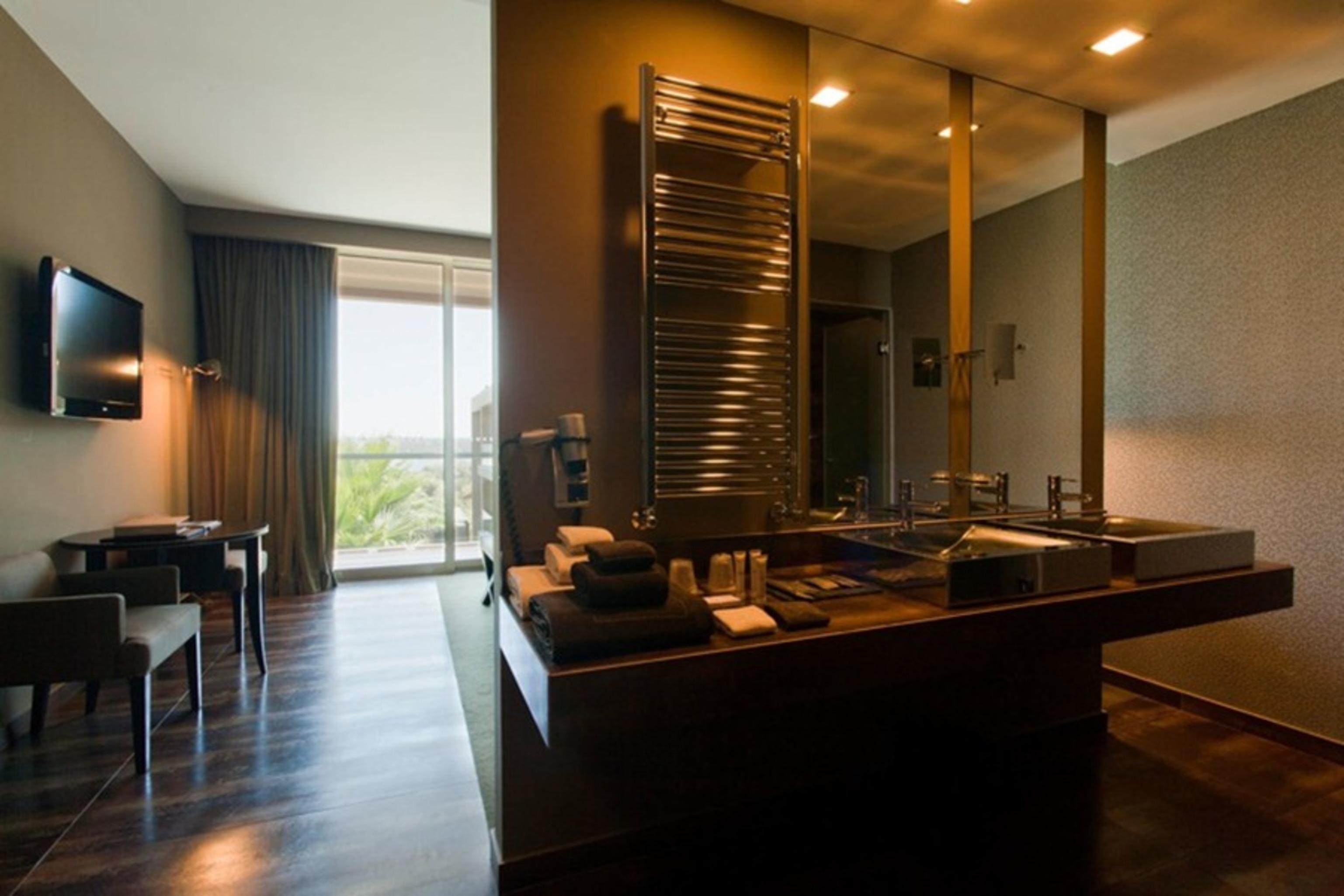 Ap Lago Montargil - Conference & Spa Eksteriør billede The photo displays a modern hotel room with a contemporary design. The room features a large window, allowing natural light to enter and offering a view outside. On one side, there is a sitting area with a small table and chairs. The other side showc