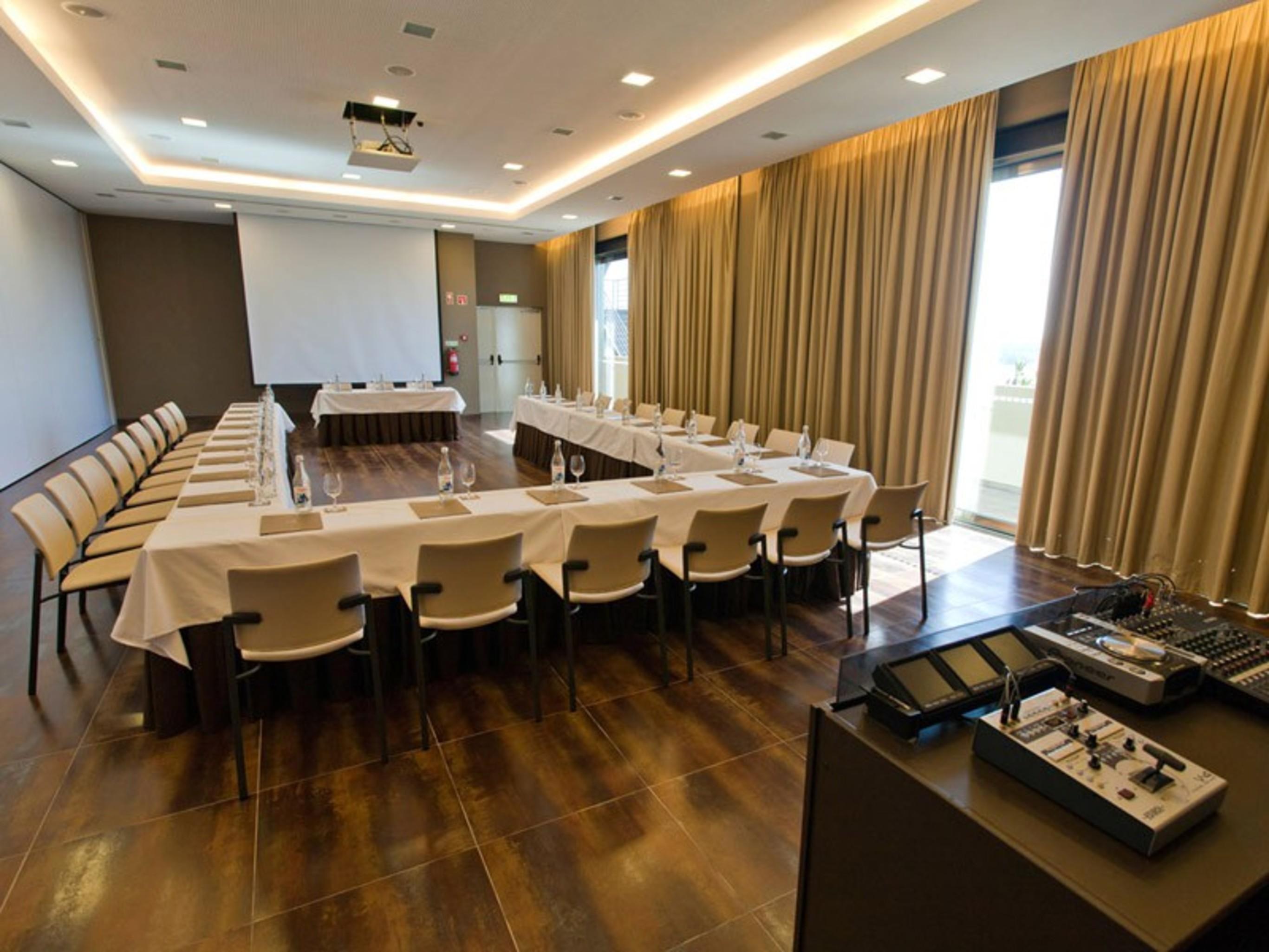 Ap Lago Montargil - Conference & Spa Eksteriør billede The photo shows a modern conference room set up for a meeting. There are several tables arranged in a U-shape, surrounded by chairs. A large screen and projector are positioned at the front, with a table for speakers or presenters. The room has large