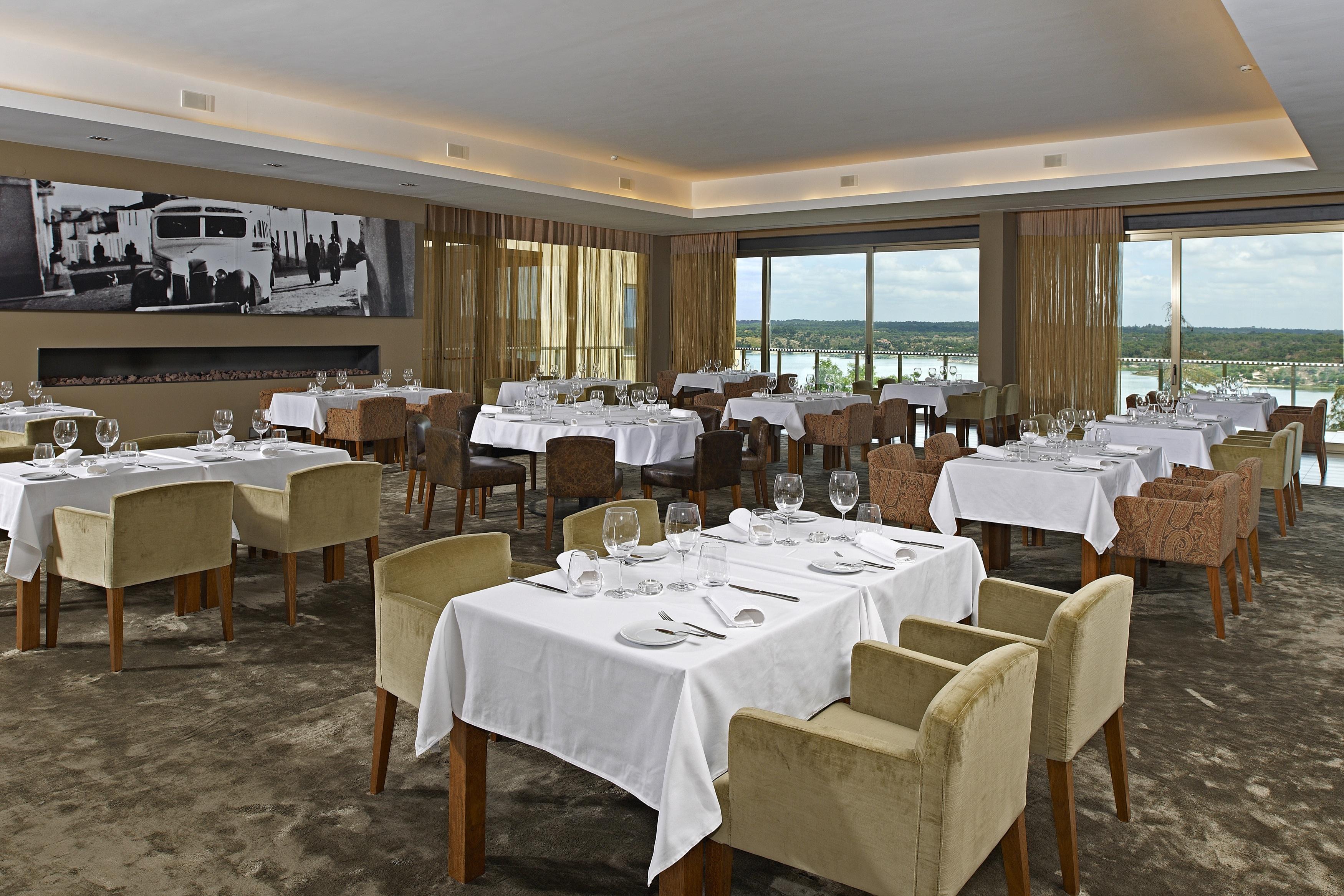 Ap Lago Montargil - Conference & Spa Eksteriør billede The photo shows an elegant restaurant interior featuring neatly arranged tables with white tablecloths. Each table is set with plates, cutlery, and glasses. The seating includes a mix of upholstered chairs in different colors—some light and others da