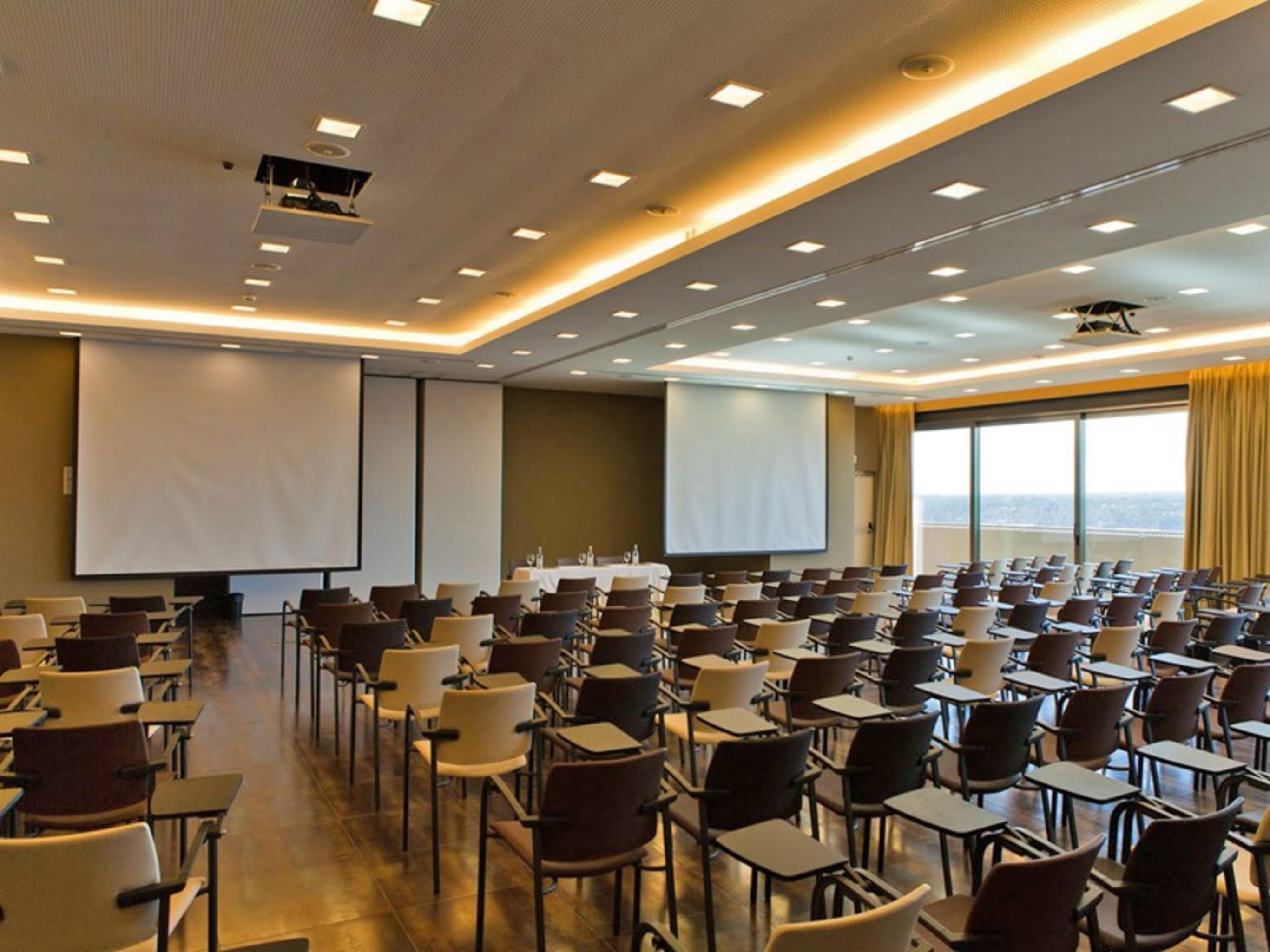 Ap Lago Montargil - Conference & Spa Eksteriør billede The photo shows a large conference room set up for a presentation or meeting. There are multiple rows of chairs arranged in a semi-theater style, facing two large projection screens. The room has a modern design, with soft lighting and large windows 