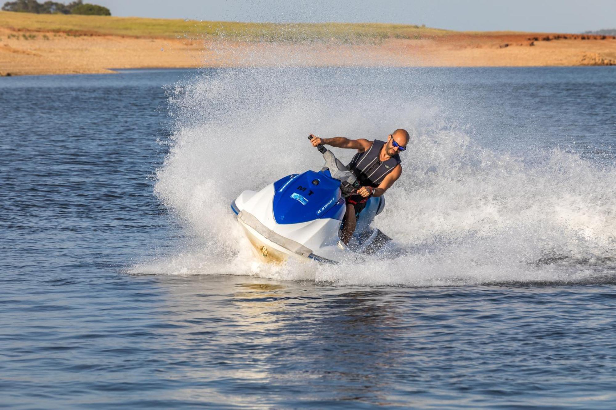 Ap Lago Montargil - Conference & Spa Eksteriør billede The photo shows a person riding a jet ski over a body of water. The rider is wearing sunglasses and a life vest, leaning forward as the jet ski accelerates, creating a spray of water around them. The background features a natural landscape, likely a 