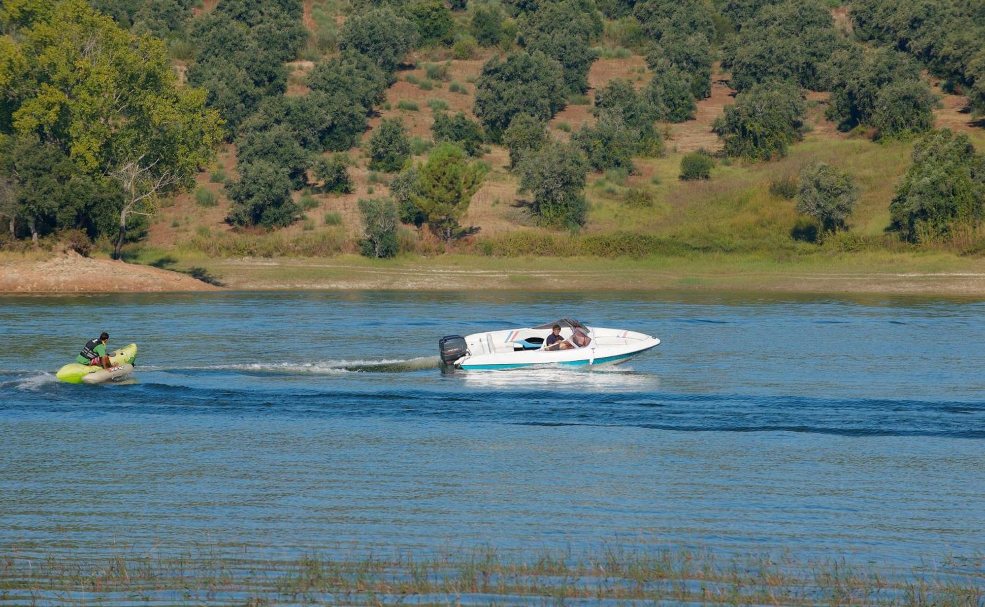 Ap Lago Montargil - Conference & Spa Eksteriør billede The photo shows a scene on a water body, likely a river or lake. In the foreground, a speedboat is moving quickly through the water, leaving a wake behind it. There are two people visible in the boat. In the background, there is a hilly area covered 