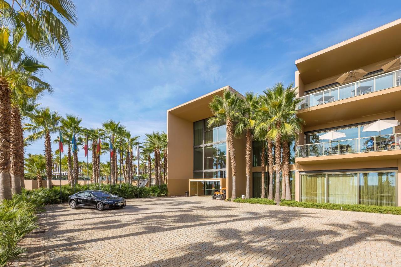 Ap Lago Montargil - Conference & Spa Eksteriør billede The photo shows a modern building with a sleek design, featuring large glass windows and balconies. The structure is surrounded by a well-maintained outdoor area with palm trees, adding a tropical feel. In front of the building, there is a paved park